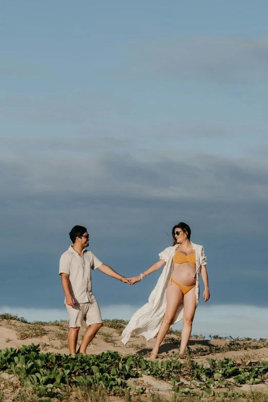 a man and a woman holding hands on a beach, pregnant belly, jin shan and ross tran, commercially ready, hills