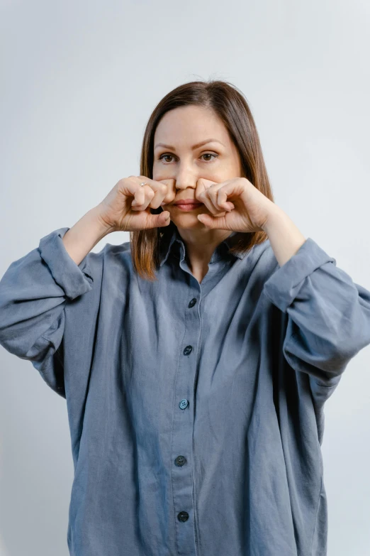 a woman making a heart sign with her hands, trending on pexels, hooked nose and square jaw, blue shirt, grey, spying discretly