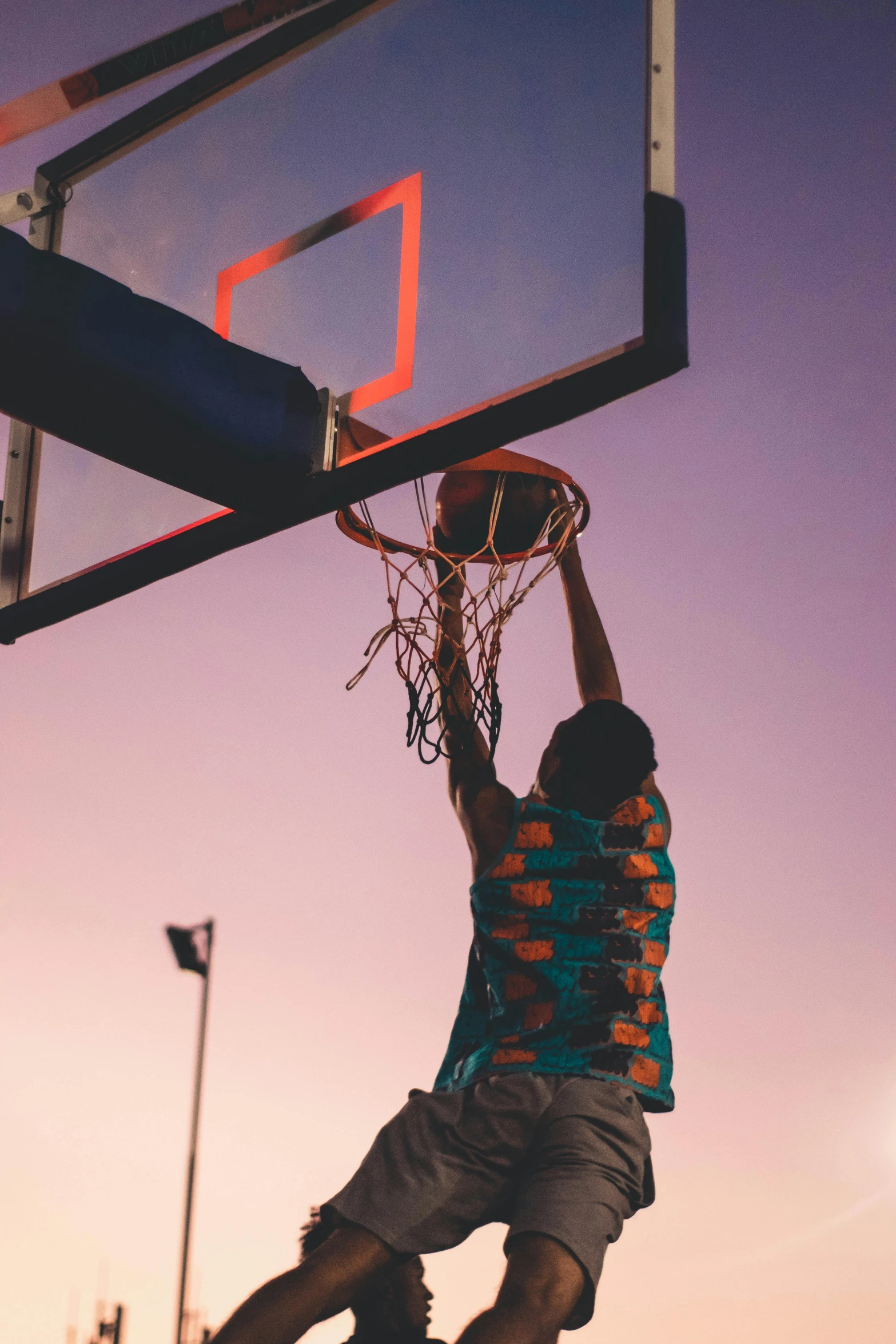 young man is reaching up to dunk a basketball in a parking lot