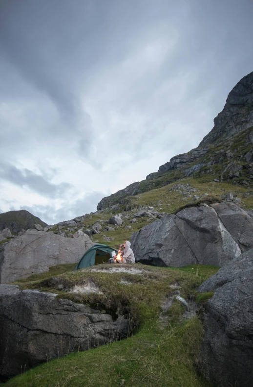 a man sitting on top of a rock next to a tent, skye meaker, fire lit, secluded, multiple stories