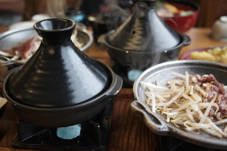 a table topped with bowls of food on top of a wooden table, unsplash, mingei, large black kettle on hearth, close up of lain iwakura, 15081959 21121991 01012000 4k, medium close up