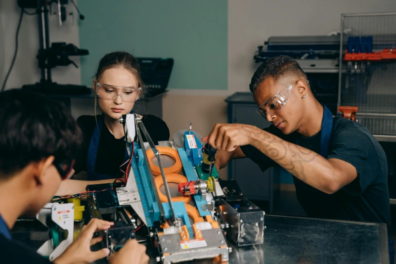 a group of people sitting around a table working on electronics, a portrait, by Adam Marczyński, pexels contest winner, high school, mechanical arm, avatar image, 278122496