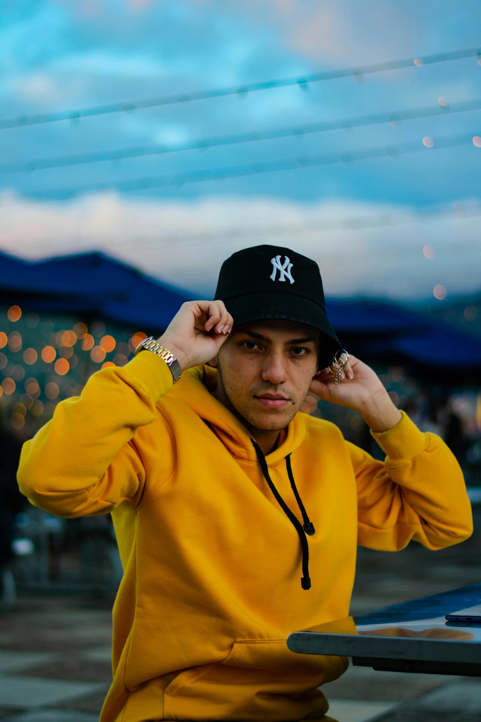 a man in a yellow hoodie sitting at a table, an album cover, unsplash, wearing baseball cap, confident pose, night setting, asher duran
