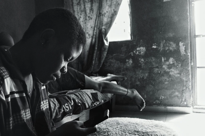 a black and white photo of a man reading a book, an album cover, by Chinwe Chukwuogo-Roy, pexels contest winner, realism, checking her phone, light over boy, at home, gunfire