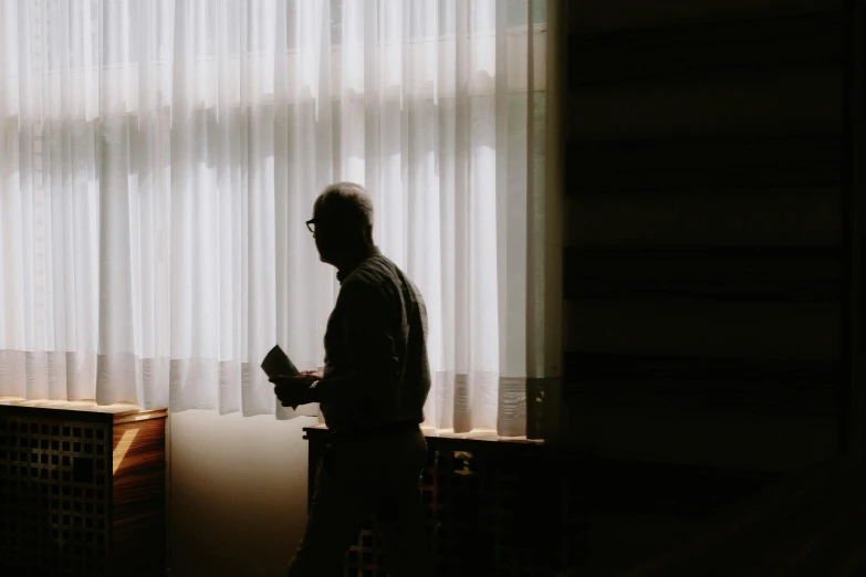 a person in a dark room next to a window looking out the curtains