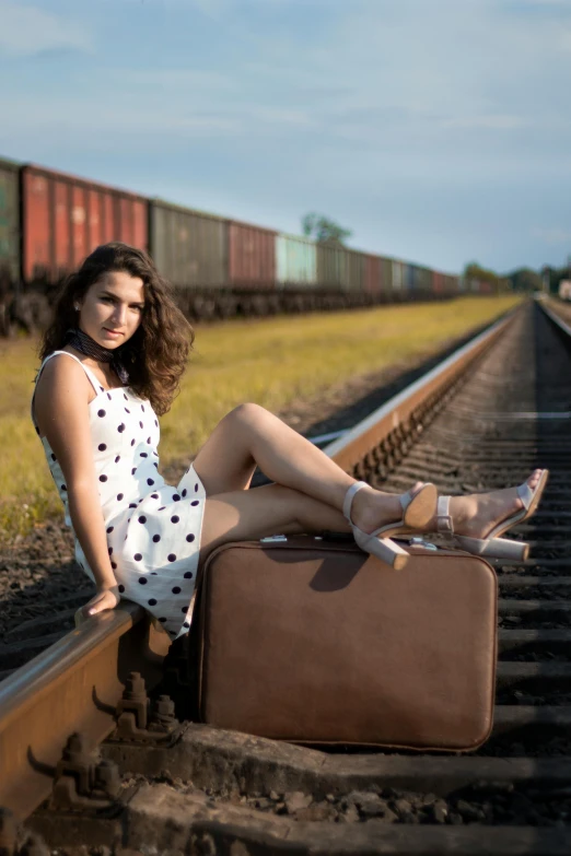 a young woman sits on railroad tracks with her luggage