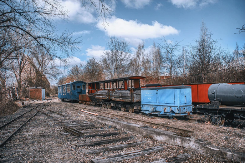 a train traveling down train tracks next to a forest, a colorized photo, by Adam Marczyński, rusty vehicles, sky blue, post - soviet courtyard, full frame image