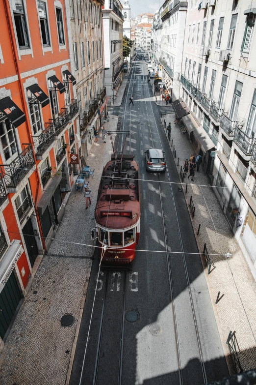 a red trolley traveling down a street next to tall buildings, pexels contest winner, happening, lisbon, high view, brown, grey