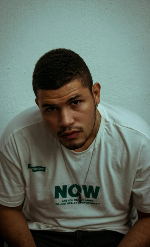 a man in white shirt sitting down wearing a necklace