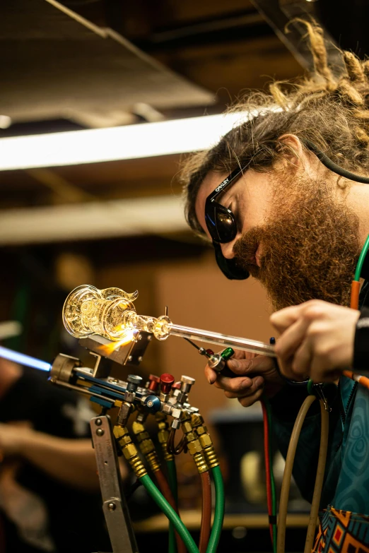 a man with dreadlocks working on a piece of glass, wearing victorian brass goggles, lachlan bailey, holding a torch, thomas veyrat intricate