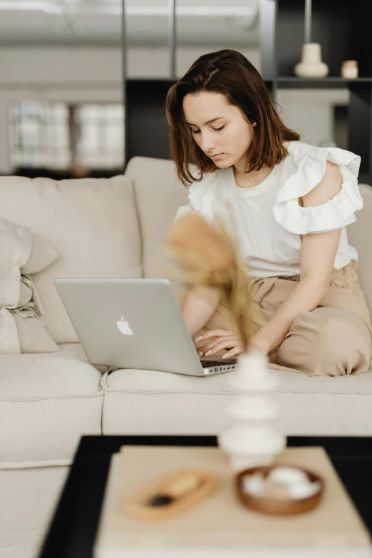 a woman sitting on a couch using a laptop, by Nicolette Macnamara, trending on pexels, renaissance, wearing a white blouse, avatar image, maintenance, brown