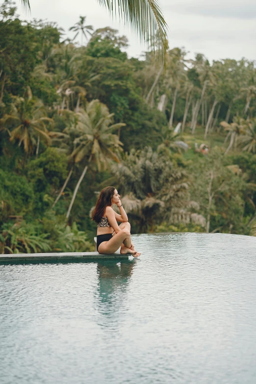 a woman sitting on the edge of a swimming pool, unsplash, sumatraism, sitting in a tree, lush vista, multiple stories, jen atkin