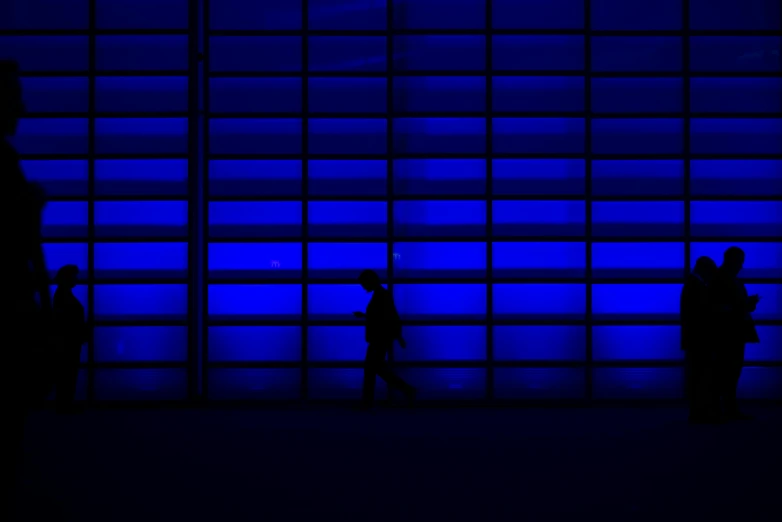 a group of people that are standing in front of a wall, inspired by Andreas Gursky, unsplash, glowing blue by greg rutkowski, man walking through city, dark. no text, cobalt blue