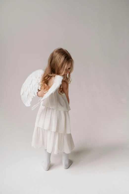 a little girl in a white dress and angel wings, pexels, in a white boho style studio, looking off to the side, profile posing, holiday season