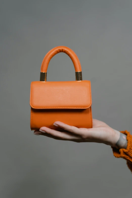 a person holding an orange purse in their hand, an album cover, by Emma Andijewska, trending on pexels, square, 70mm, exquisite handle, handbag