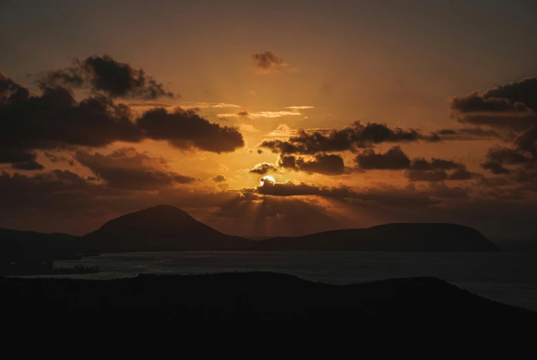 an orange sunset over the ocean and hills