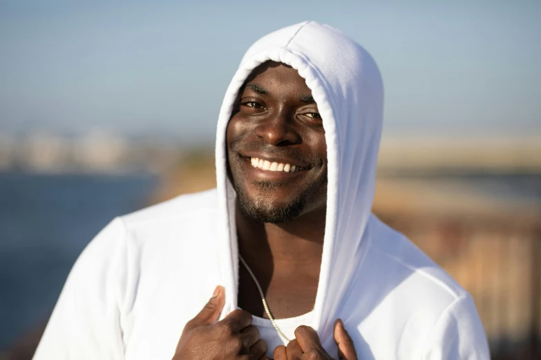 a close up of a person wearing a hoodie, pexels contest winner, brown skin man with a giant grin, white loincloth, wearing fitness gear, wearing silver silk robe