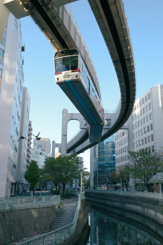 a train traveling through a city next to tall buildings, sōsaku hanga, suspended bridge!, anti - gravity, curving, opposite the lift-shaft