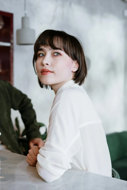 a woman sitting at a table next to a man, trending on pexels, with short hair with bangs, portrait of a female model, nadezhda tikhomirova, wearing a light shirt