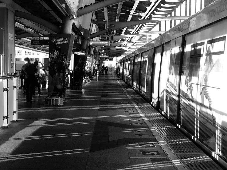 a black and white photo of a train pulling into a station, a black and white photo, by Hirosada II, flickr, minimalism, in sao paulo, beautiful sunlight and shadows, people on the ground, in neotokyo