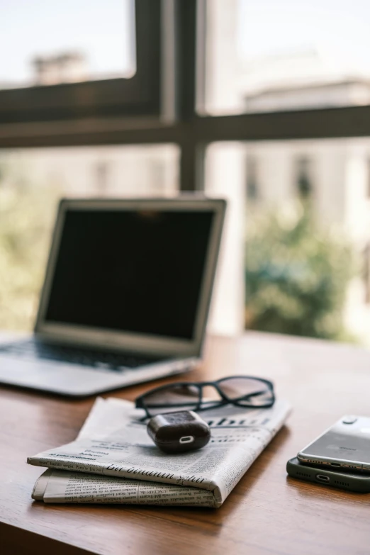 an open laptop computer sitting on top of a wooden desk, trending on pexels, reading glasses, next to a big window, low fi, news archive