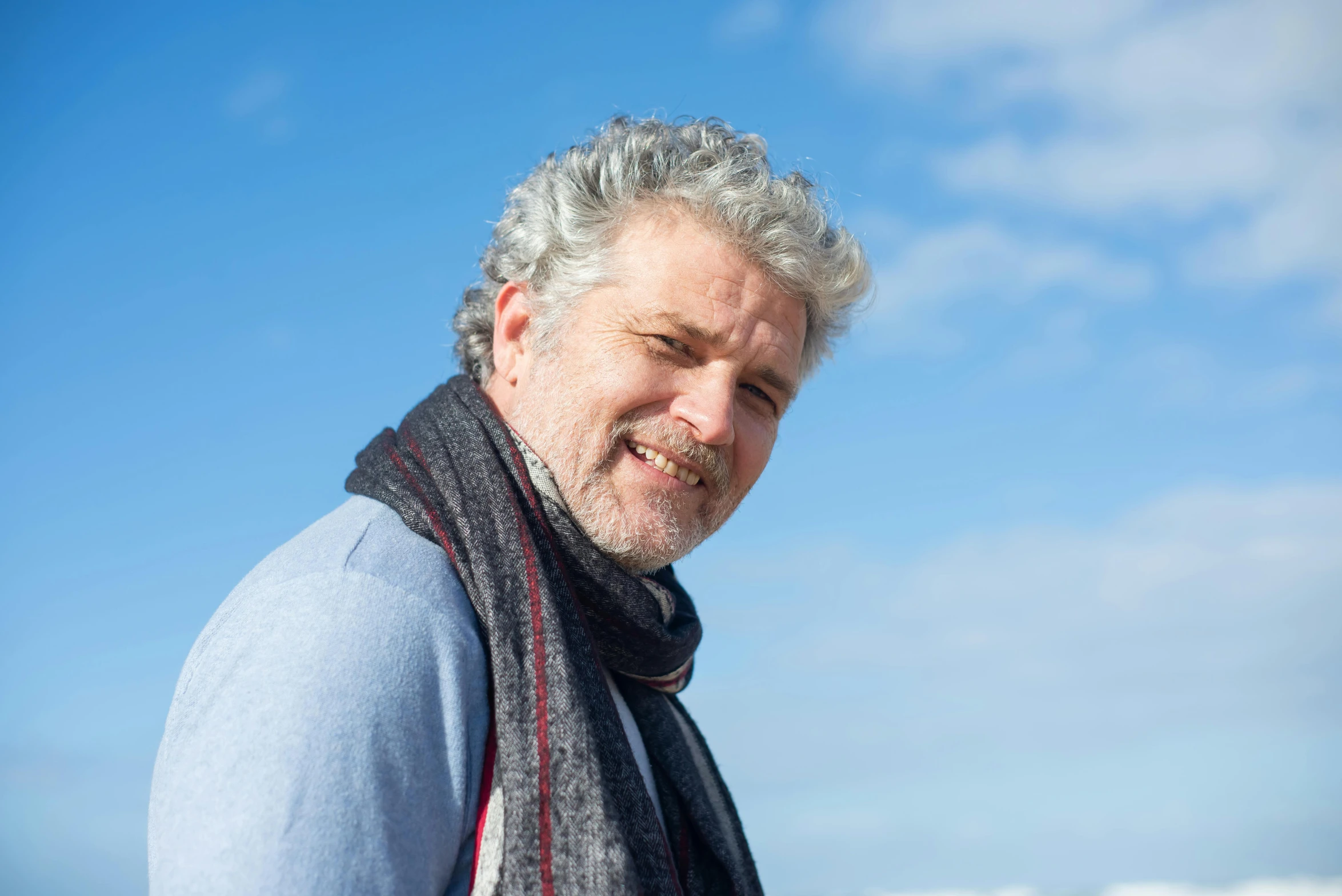 an older man with grey hair and a scarf is looking to his left