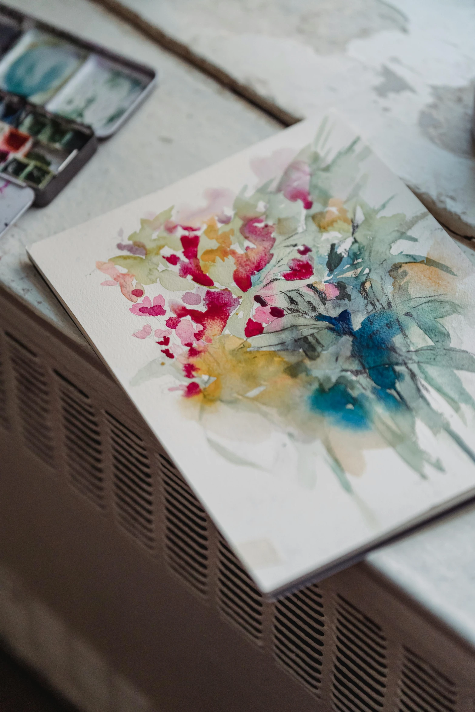 a piece of art sitting on top of a table, a watercolor painting, inspired by Richard Schmid, unsplash, floral explosion, in a studio, on a white table, unfinished