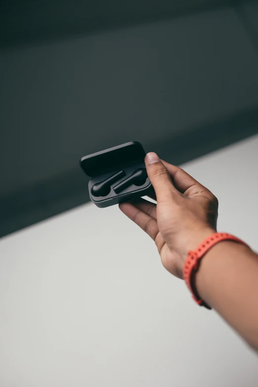 a person holding a cell phone in their hand, by Nina Hamnett, trending on pexels, minimalism, earbuds, black 3 d cuboid device, inspect in inventory image, matte surface