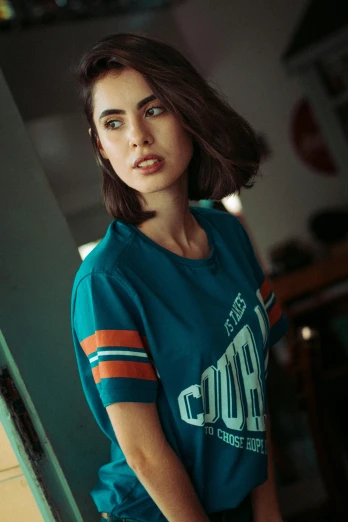 a woman in a blue shirt leaning against a wall, a colorized photo, inspired by Elsa Bleda, sport t-shirt, ana de armas portrait, orange and teal color, wearing nba jersey