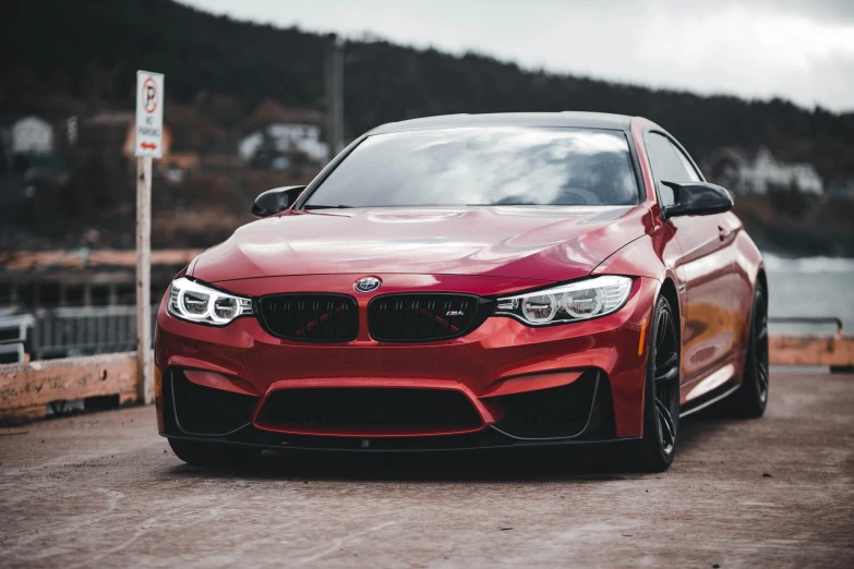 a red bmw is parked next to a lake