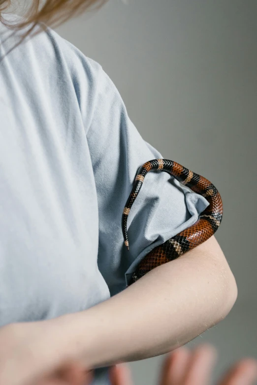 a woman in a blue shirt with a snake on her arm, an album cover, by Adam Marczyński, trending on pexels, patricia piccinini, low detail, male teenager, close-up photo