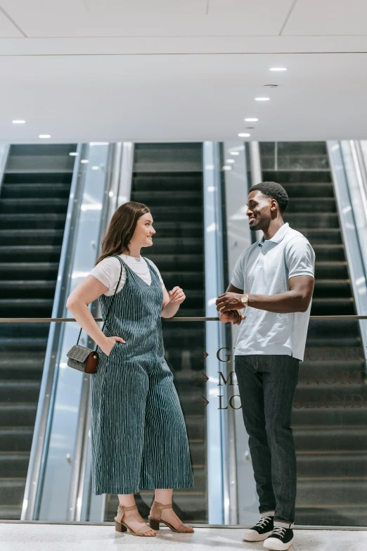 a man and a woman standing in front of an escalator, talking, overalls, gen z, no watermarks