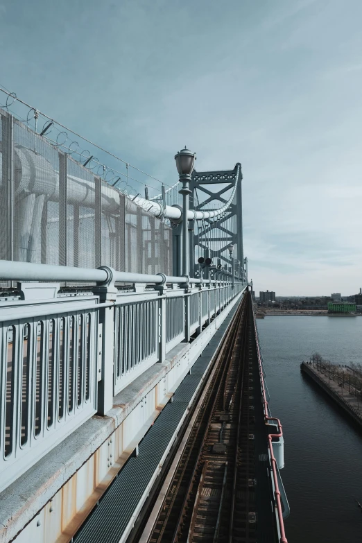 a train traveling over a bridge next to a body of water, steel pipes, towering high up over your view, industrial aesthetic, walkways