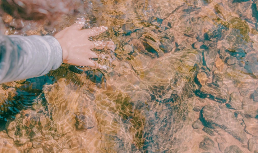 hands are held in clear water on the beach