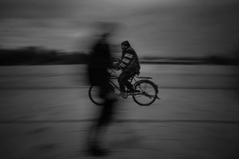 a black and white photo of a person riding a bike, by Gusztáv Kelety, pexels contest winner, conceptual art, very blurry, on the frozen danube, shadowy and eerie character, high quality upload