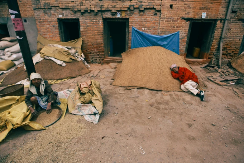 a man laying on the ground next to a pile of sand, trending on unsplash, arte povera, nepali architecture buildings, rice, covered with blanket, 1990's photo