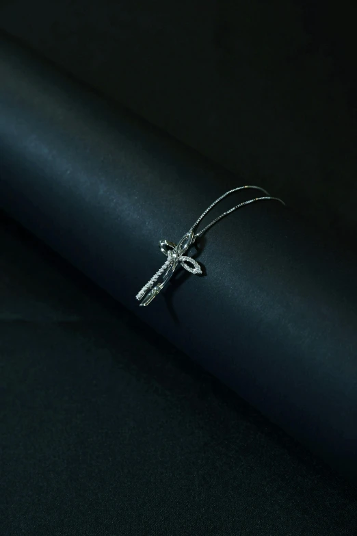 a close up of a ring on a black surface, an album cover, inspired by Cerith Wyn Evans, trending on reddit, hurufiyya, dragonfly, crucifix, silver necklace, detailed photograph high quality