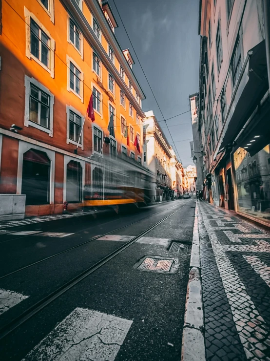 a yellow train traveling down a street next to tall buildings, pexels contest winner, portugal, gray and orange colours, square, warm street lights store front