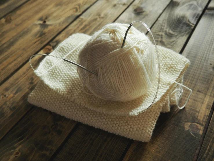 a ball of yarn sitting on top of a wooden table, white clothes, cream and white color scheme, getty images, thumbnail