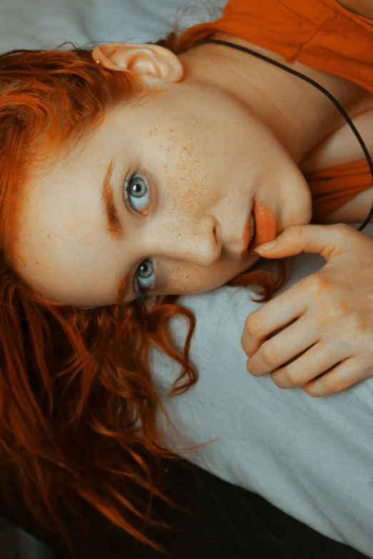 a beautiful young woman laying on top of a bed, inspired by Elsa Bleda, trending on pexels, renaissance, red hair and freckles, gif, concerned, orange pupils