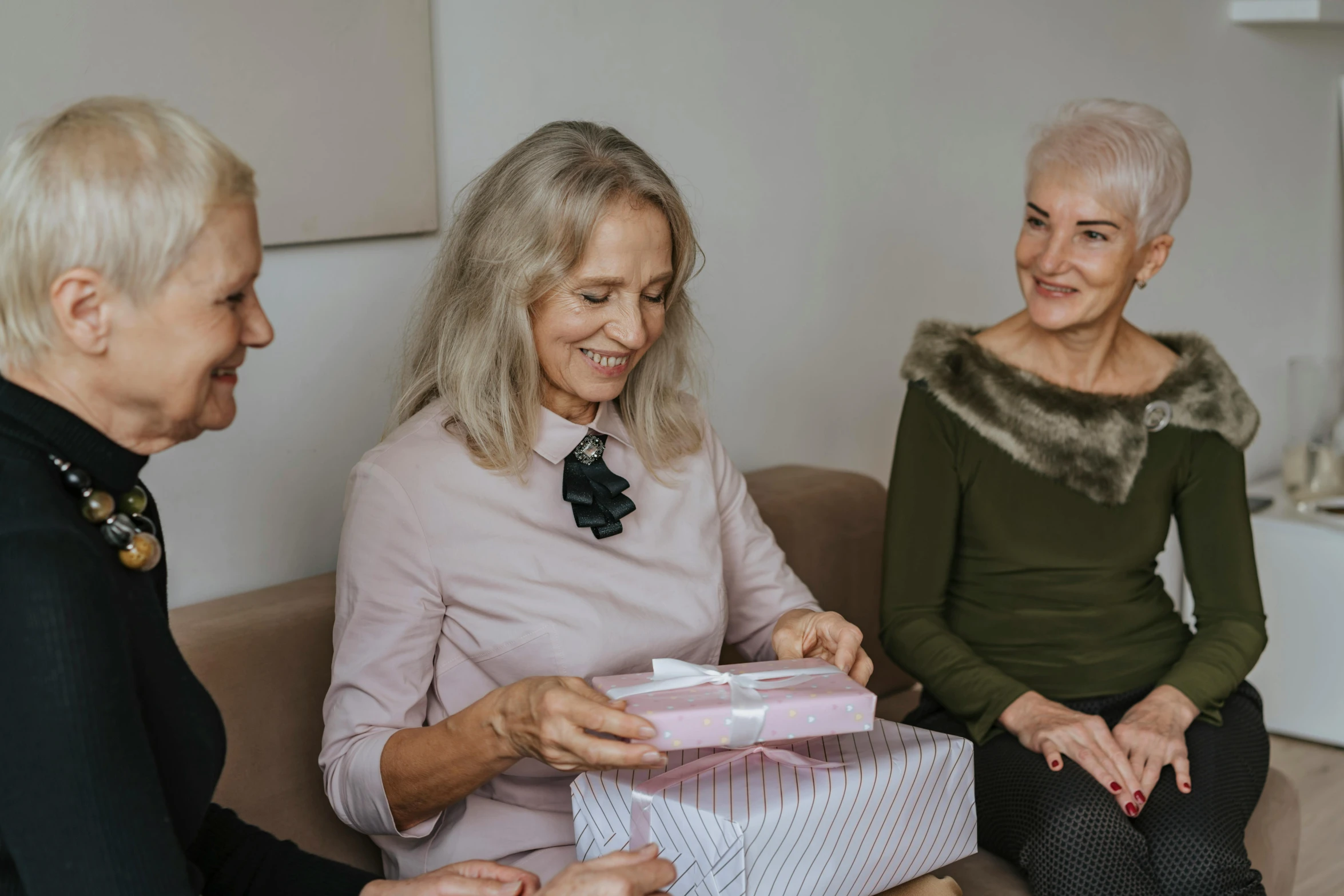 a group of older women sitting on top of a couch, by Emma Andijewska, pexels contest winner, holding gift, on a white table, three women, looking to the right