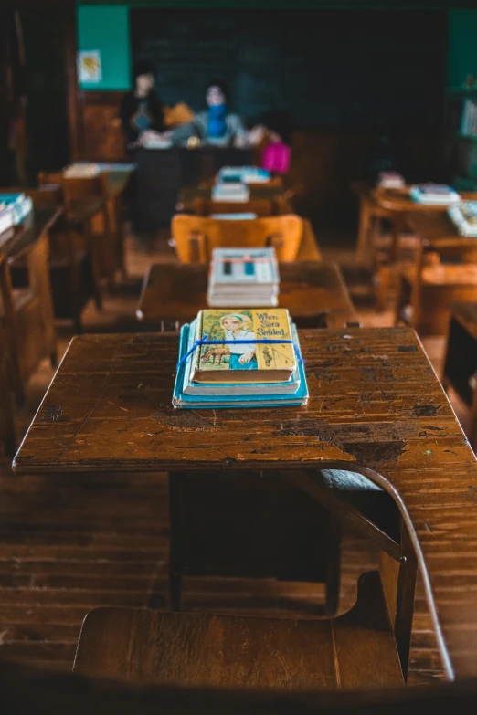 a book sitting on top of a wooden table, in a classroom, multiple desks, old school, paul barson