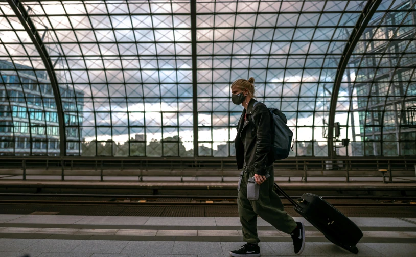 a man walking with a suitcase at a train station, by Tobias Stimmer, happening, white man with black fabric mask, adventurer, afp, a blond