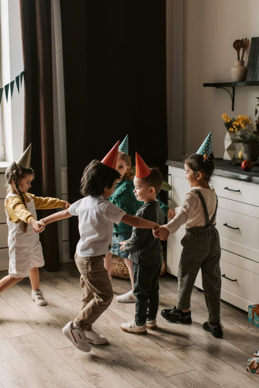 a group of children holding hands in a room, by Adam Marczyński, pexels contest winner, arts and crafts movement, party hats, playful pose, promo image, pals have a birthday party