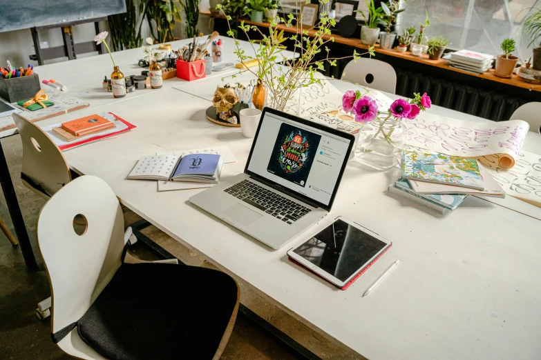 a table topped with a laptop computer next to flower pots and a lamp