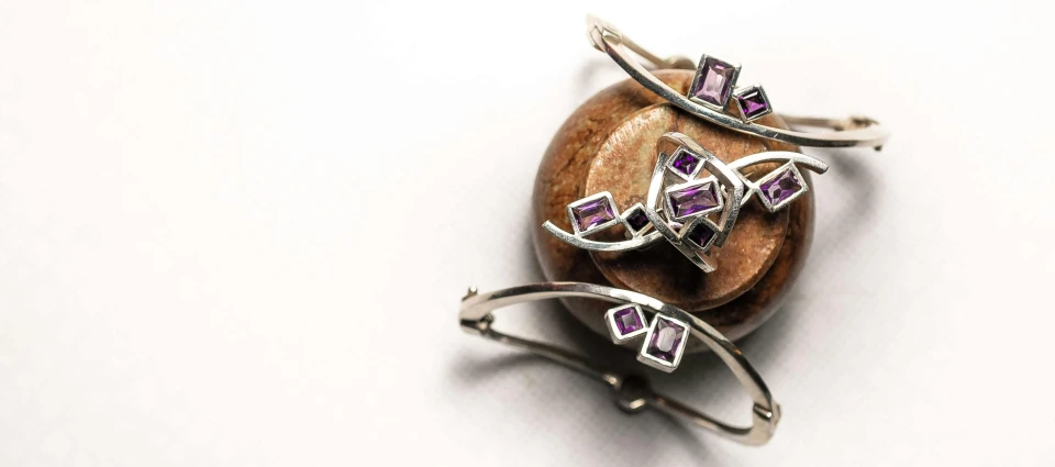 a couple of rings sitting on top of a rock, trending on cg society, art nouveau, silver and amethyst, shungite bangle, geometrical, high quality product image”