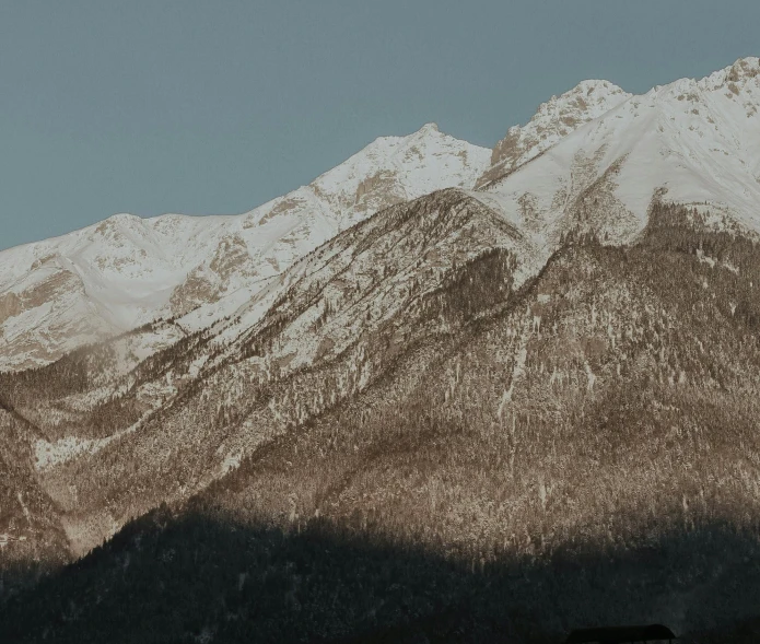 two horses graze in front of snow - capped mountains