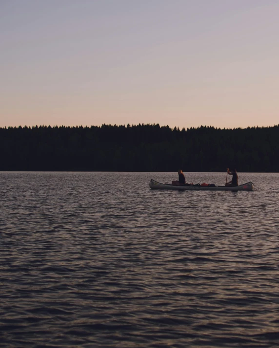 a couple of people in a boat on a lake, in the evening, body of water, it has a lake in the distance