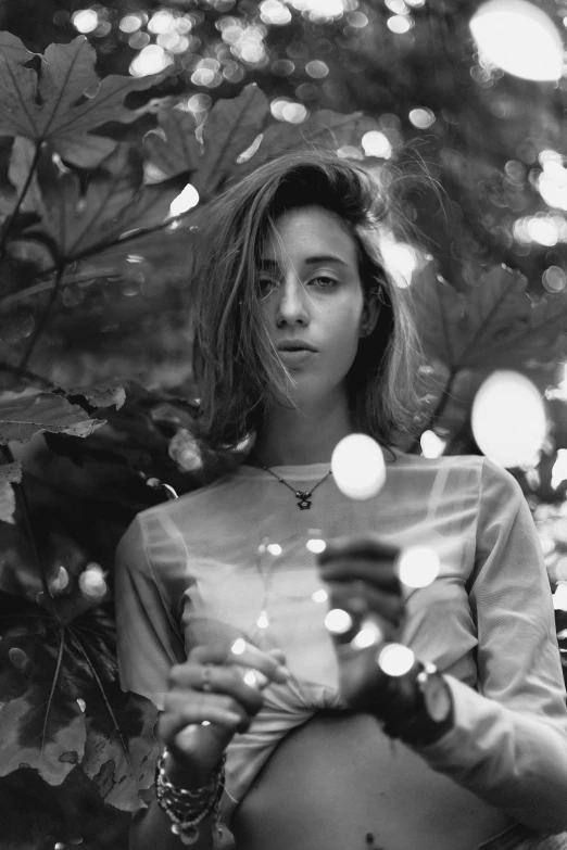 a black and white photo of a woman holding a cell phone, tumblr, magical realism, ana de armas portrait, in a candy forest! at night, androgynous person, analogue photo low quality