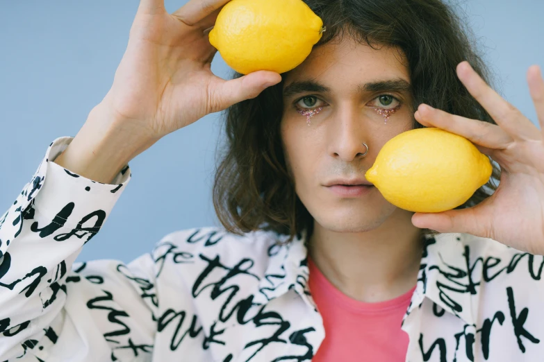 a man holding two lemons in front of his face, an album cover, by Adam Dario Keel, trending on pexels, magic realism, jonny greenwood, looking to the side off camera, lily frank, 🍸🍋